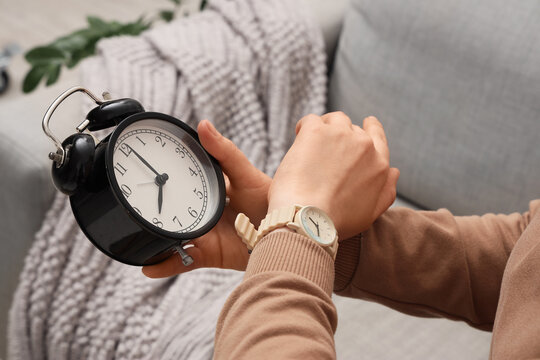 Female hands with wristwatch and alarm clock at home, closeup. Daylight saving time concept