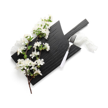 Black wooden cutting board with fork and beautiful blooming tree branch on white background