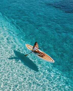 Paddleboarder gliding on clear turquoise shallows from drone shot