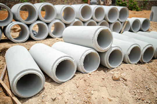 Concrete drainage pipes with small diameter fill foreground while larger bore sections stand behind, layered arrangement shows range of storm water pipe sizes staged at construction lot