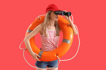 Young female lifeguard in cap with rescue ring looking in binocular on red background © Pixel-Shot