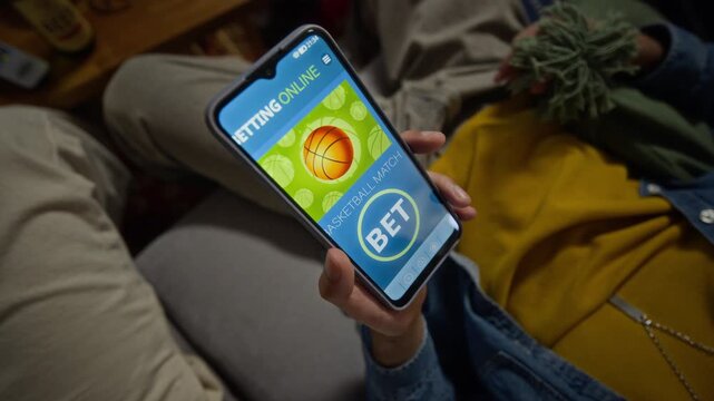 Middle Eastern young adult man holding smartphone displaying online sports betting app beside African American friend. Clip suited for mobile gambling marketing and digital sports fan campaigns