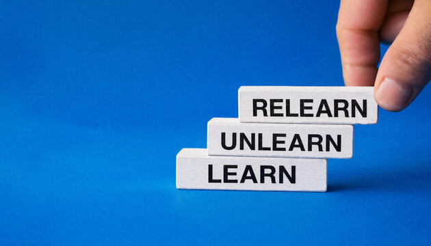 Hand placing wooden block with relearn text on top of unlearn and learn blocks against blue background symbolizing continuous learning concept