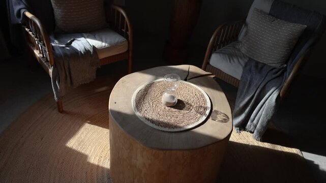 Small glass hourglass filled with sand stands on a woven mat atop a natural wooden table, illuminated by warm sunlight in a cozy rustic interior