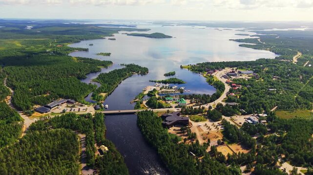 Aerial panorama over Inari in Finnish Lapland, where forested peninsulas, scattered buildings and calm waterways open toward the vast island-dotted expanse of Lake Inari.