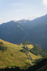 Obraz premium Alpine Mountain Landscape with Winding Asphalt Road Illuminated by Evening Sunlight