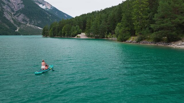 A person stand up paddleboards across clear turquoise water on Achen Lake in Tyrol, Austria, surrounded by an alpine mountain landscape