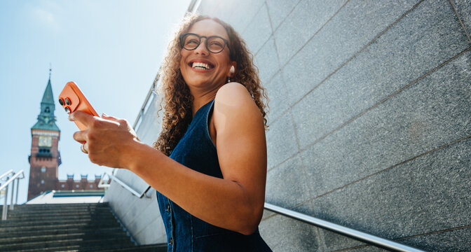 Smiling woman ascends city stairs checking smartphone outdoors