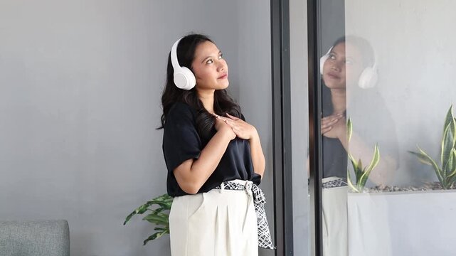 Relieved young asian woman with headphones enjoying morning at home