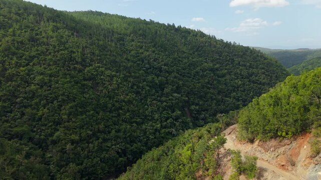 Drone footage traveling forward above dense vegetation and mountain terrain across the future Guaigui Dam reservoir area in La Vega Dominican Republic