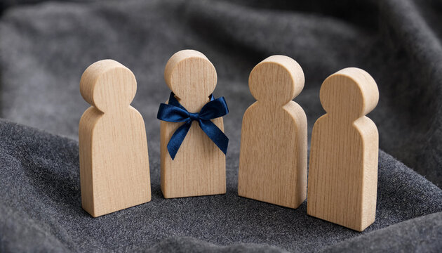 Recognition concept with wooden figures one adorned with blue ribbon on gray fabric background