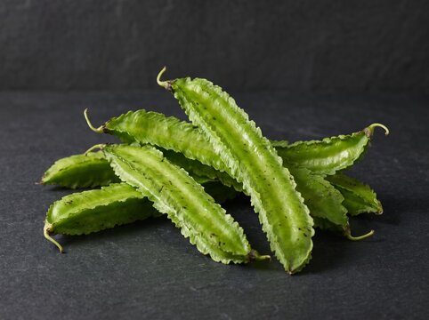 Fresh kecipir winged bean pods with frilled edges on dark stone background