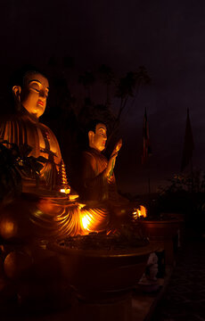 Two serene sitting Buddha statues with colorful Buddhist flags at Chua Da Bao Pagoda in Nha Trang, Vietnam. Peaceful spiritual scene in a traditional temple at night time