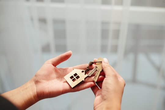 Hands holding new house keys with wooden keychain