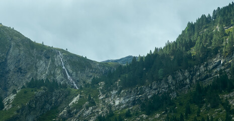 serene mountain landscape with cascading waterfall and rugged terrain under a cloudy sky, aerial...