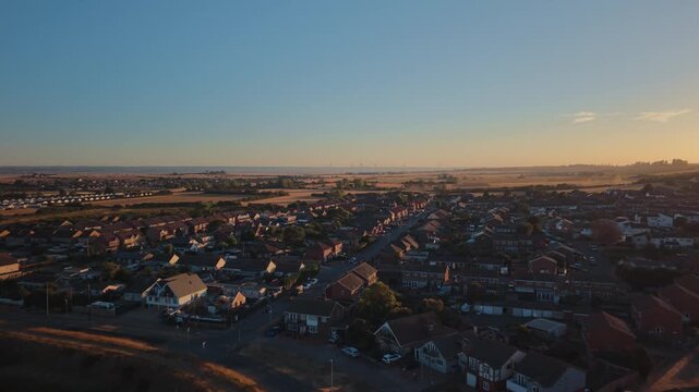 Leysdown-on-Sea on the Isle of Sheppey, Kent, after the partial solar eclipse, with residential streets and coastline in warm evening light, wide aerial view