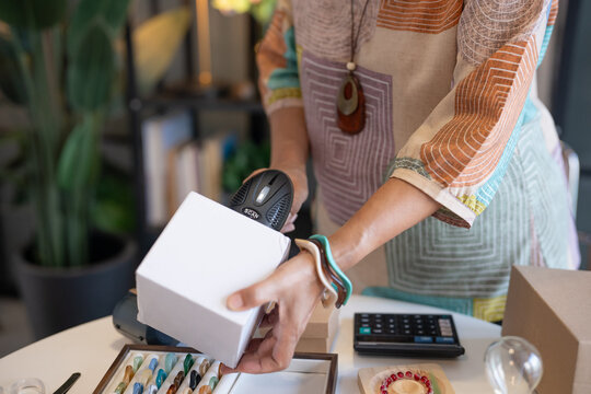 woman scanning product barcode with handheld scanner at handmade retail shop using technology small business management.