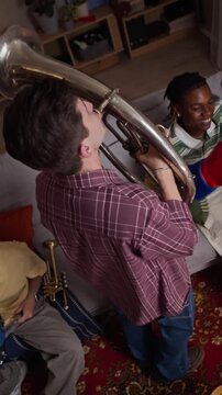 Vertical shot of young Caucasian man playing brass horn with diverse male friends celebrating sports game at home. Footage suitable for football fandom campaigns and streaming ads