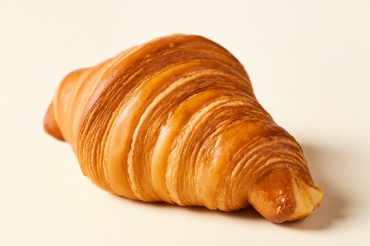 Fresh croissant laying on a flat beige surface viewed from an angle