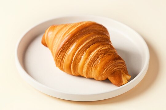 Fresh croissant laying on a beige plate viewed from an angle. Beige background