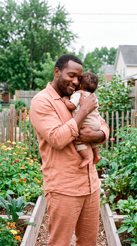Happy father embracing his newborn baby in a blooming backyard vegetable garden
