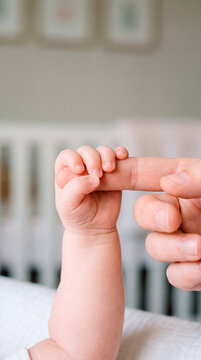 Newborn baby gripping a parent's finger tightly while resting inside the crib