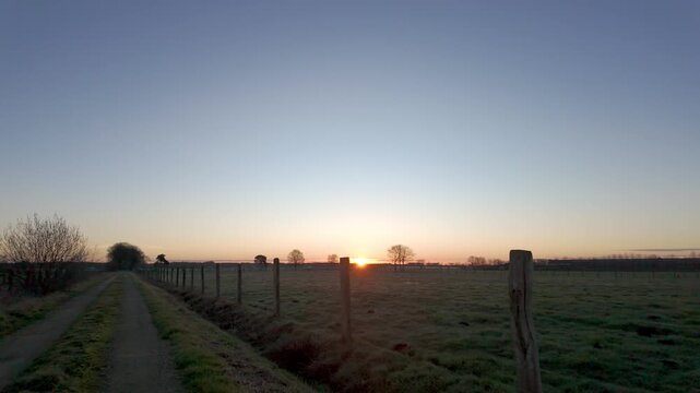 Slow pull-back shot of a beautiful sunrise over a peaceful rural field and country lane