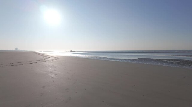 Cinematic forward motion over a serene, empty beach at sunrise with bright sun and calm ocean waves.
