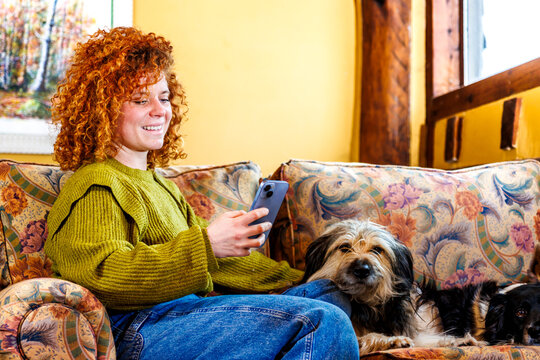 Redhead woman enjoying social media on smartphone while relaxing with dogs