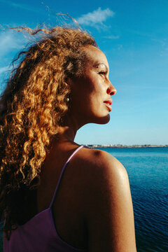 Woman enjoys sunlight on face while gazing over the sea
