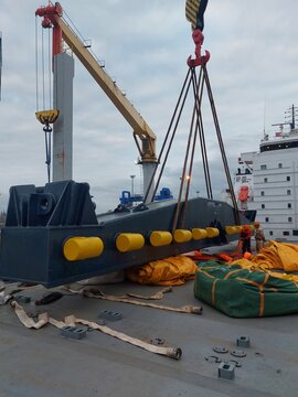 Heavy lift operation on cargo vessel deck with crane lifting massive spreader beam and rigging gear