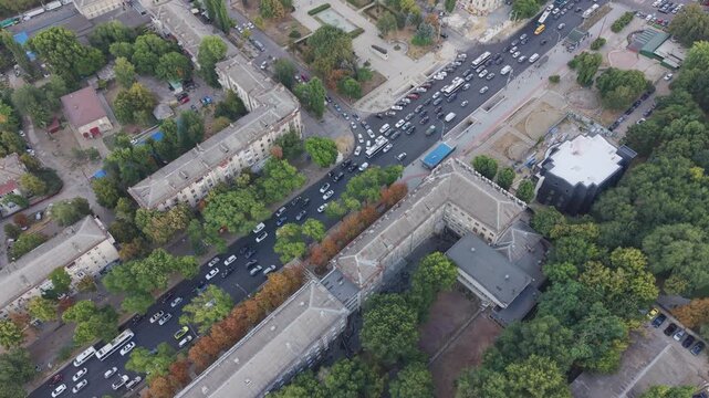 Aerial drone view of heavy traffic on a busy street in Chisinau, Moldova, showing cars and buses moving through a congested urban road and intersection surrounded by buildings and trees.