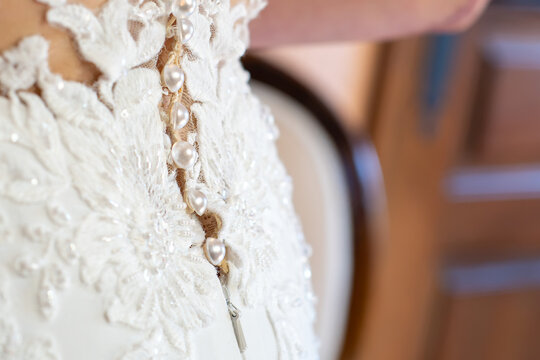 Close up detail of the back of a white wedding dress with pearl buttons, zipper and delicate floral lace embroidery with beads and sequins, elegant bridal gown craftsmanship on wedding day morning