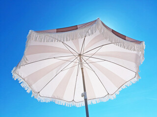 Beach umbrella with white and yellow strips with blue sky background. © Iryna
