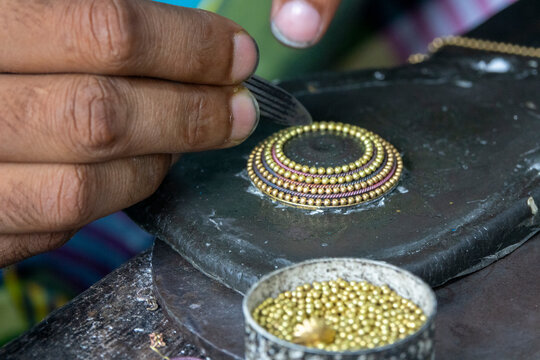 Metal worker's hands applying tiny gold beads to a circular jewelry piece using the lost wax casting method, Dhaka Division, Dhamrai, Bangladesh