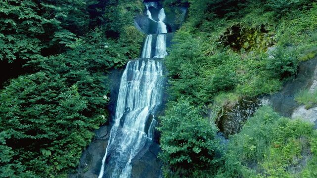 The impressive Kevin Mountain Waterfall, flowing down rocky ledges into a clear stream, surrounded by dense green forest and lush summer foliage in the calm, picturesque wilderness of Georgia