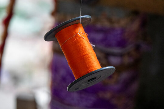 Spool of orange silk thread hanging above woven fabric, Dhaka Division, Delduar, Bangladesh