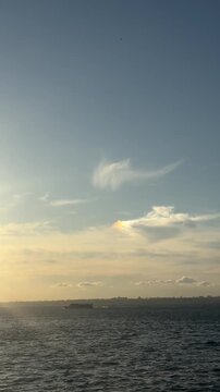 Passenger boat on sea with iridescent cloud and rainbow sky vertical video.