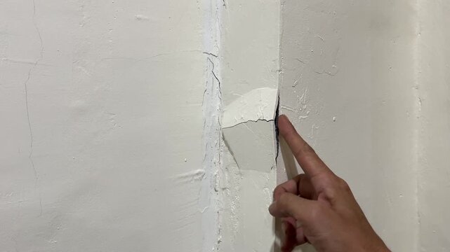Hand touching peeling plaster on cracked corner wall