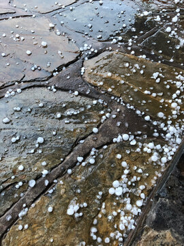 Hailstones scattered across wet, textured flagstone pavers, creating a striking contrast and symbolizing changing weather