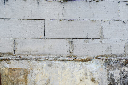 Raw grey aerated concrete block wall texture with dripping mortar and dark stained cement foundation.