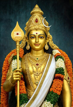 Golden statue of Hindu deity with ornate jewelry and floral decorations holding a trident