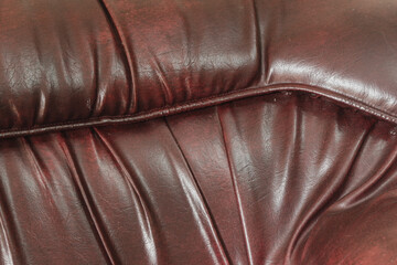 Dark reddish brown faux leather upholstery texture with deep creases and stitched seam. © Jassem