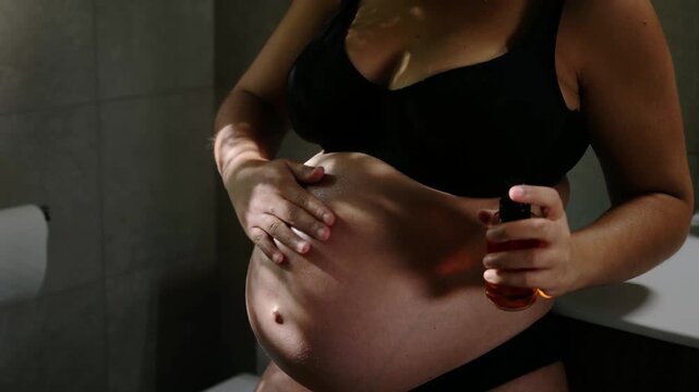Expectant mother moisturizing her tummy to prevent stretch marks in the bathroom