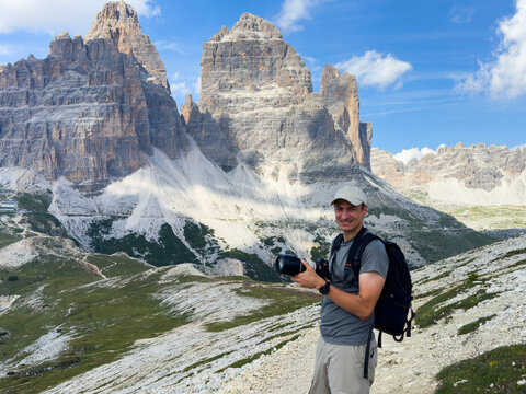 photographer posing with camera on rocky mountain landscape, happy and adventurous mood from a higher vantage point with grass and gray tones, natural light and clean background for travel.