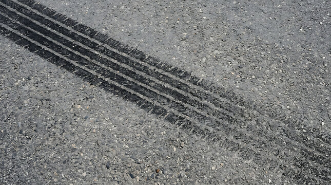 Detailed close-up view of clear black tire skid marks on gray asphalt road surface