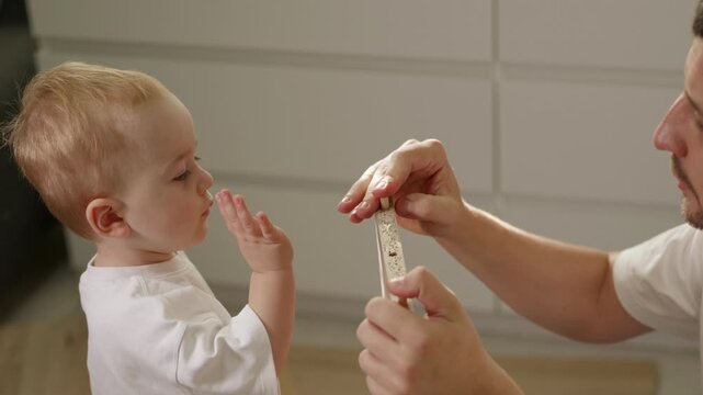 Father and toddler interact while assembling furniture at home, with the child reaching for a toy airplane and the parent holding a wooden piece in a bright indoor setting