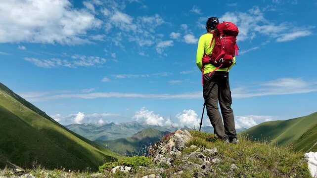 A hiker with backpack and trekking poles stands on a rocky mountain ridge, overlooking a sweeping alpine valley under a bright blue sky, conveying adventure, freedom, and exploration.