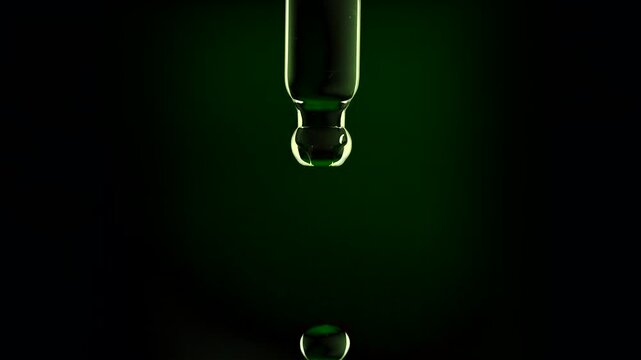 Macro shot of a natural aloe vera extract or tea tree oil droplet falling from a glass pipette dropper in slow motion isolated on a dark background