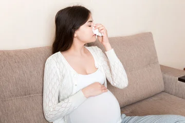 Sick pregnant woman blowing nose into tissue at home Healthy millennial healthcare concept © sosiukin